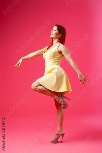 Young seductive woman in a yellow dress in the style of a new look swirls, poses and has fun on a pink isolated background. The concept of female beauty and grace, posing in a photo studio