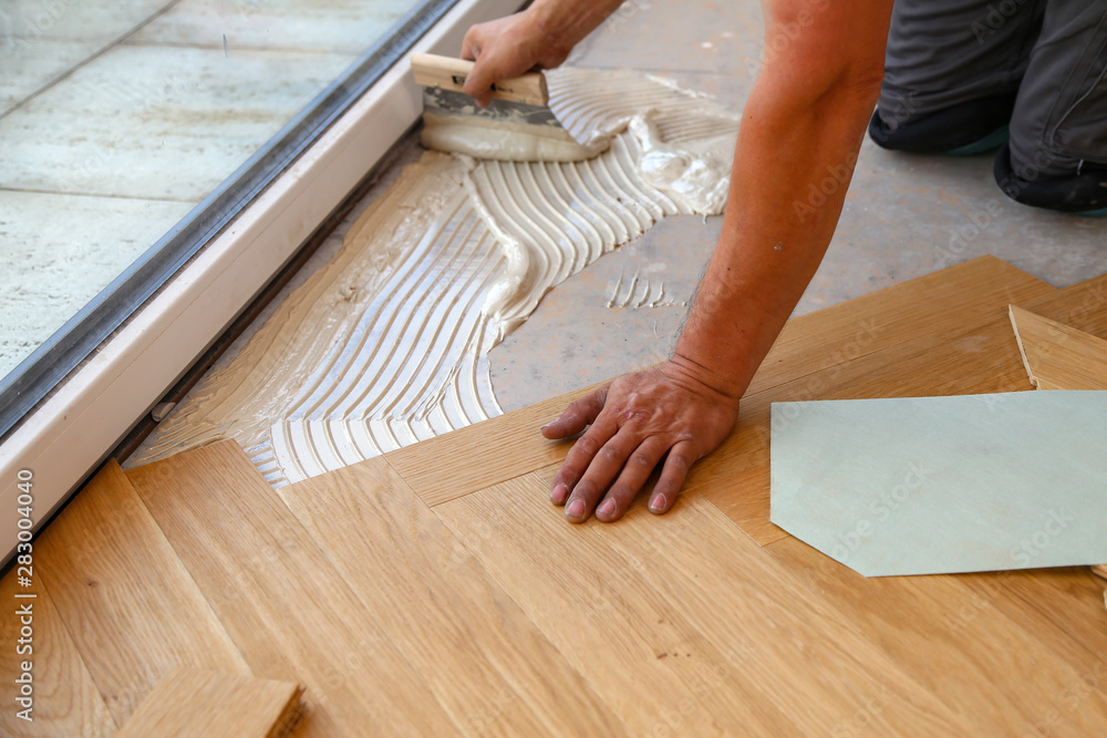 Worker laying parquet flooring. Worker installing wooden laminate flooring - obrazy, fototapety, plakaty 
