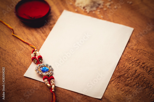 Rakhi With Kumkum, Rice Grains And A White Paper On A Wooden Surface