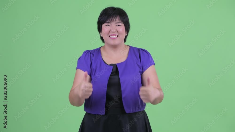 Happy young overweight Asian woman giving thumbs up and looking excited Happy young overweight Asian woman giving thumbs up and looking excited