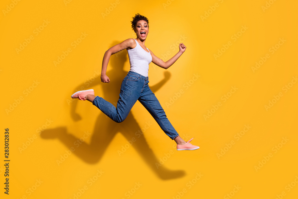Full length side profile body size photo funny she her dark skin model lady jumping high champion rush sale discount shop wear casual jeans denim pants trousers tank-top isolated yellow background - obrazy, fototapety, plakaty 