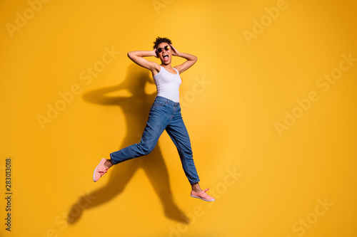 Full length side profile body size photo beautiful she her dark skin lady jumping high yell yeah triumphant champion wear casual jeans denim pants trousers tank-top isolated bright yellow background