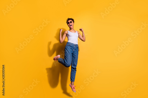 Full length body size photo beautiful she her dark skin excited lady jumping high yell yeah yes triumphant champion wear casual jeans denim pants trousers tank-top isolated bright yellow background