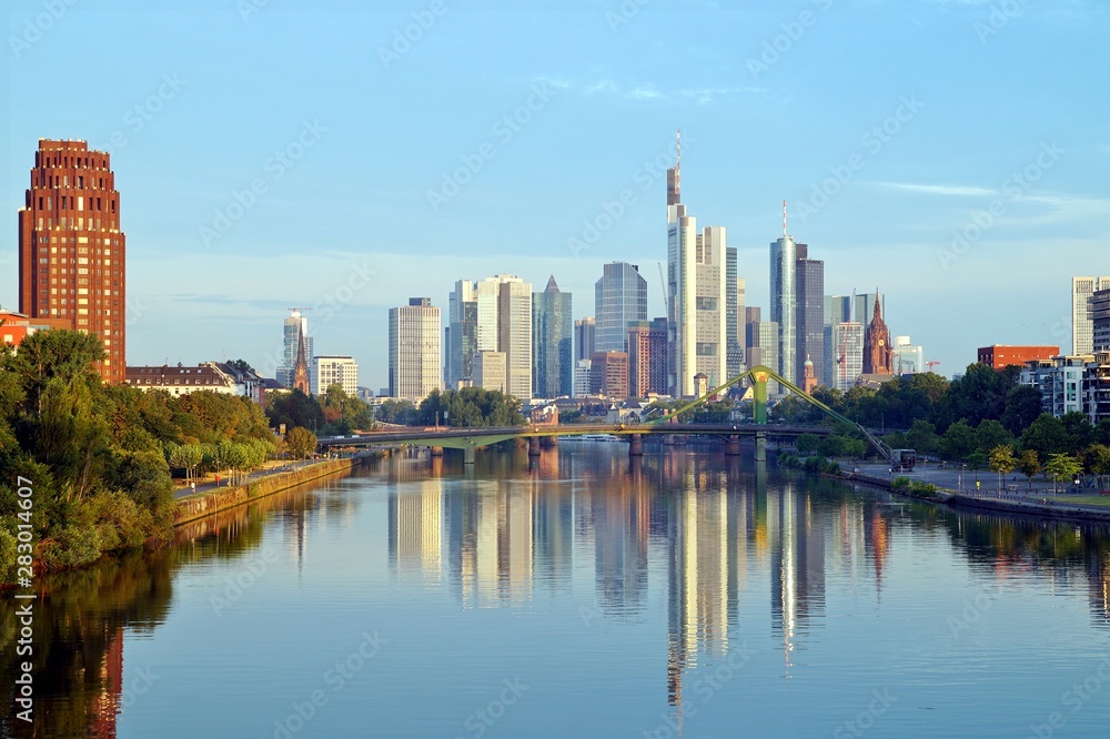Fototapeta premium Skyline Frankfurtu odbijający się w rzece Men o wschodzie słońca. europejska panorama miasta i finansowe centrum Frankfurtu. Niemcy Wieżowiec budynki na tle niebieskiego nieba. Koncepcja biznesu i finansów