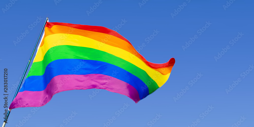 Gay rainbow flag waving in the wind in a clear blue sky Gay rainbow flag waving in the wind in a clear blue sky