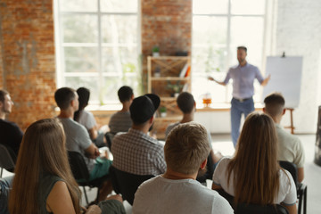 Male speaker giving presentation in hall at university workshop. Audience or conference hall. Rear view of unrecognized participants in audience. Scientific conference event, training. Education