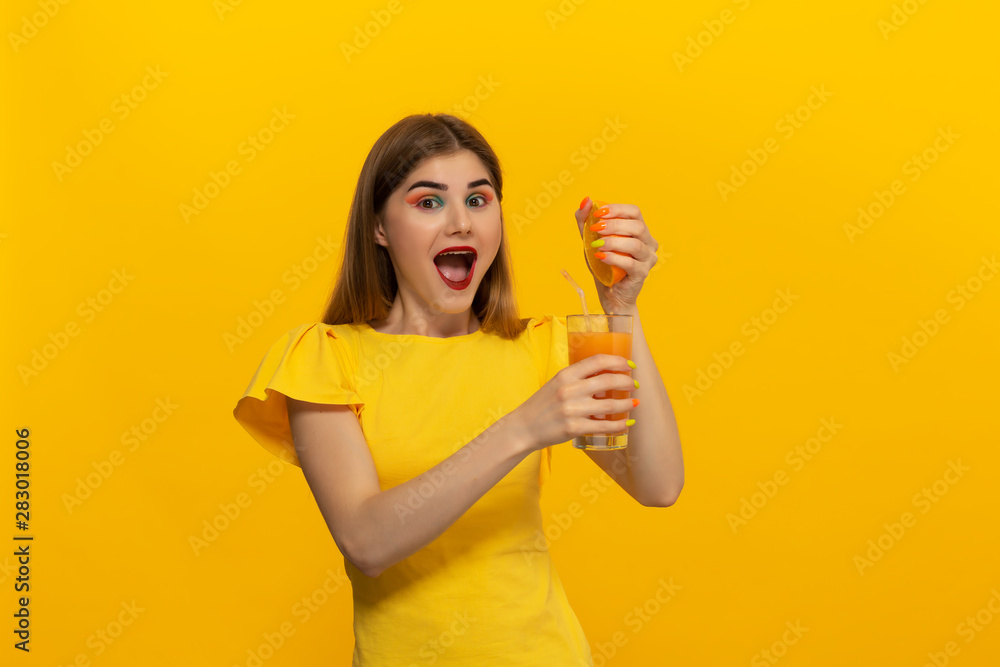 Close-up portrait of a beautiful young girl squashing orange juice into glass isolated over yellow background. Close-up portrait of a beautiful young girl squashing orange juice into glass isolated over yellow background.