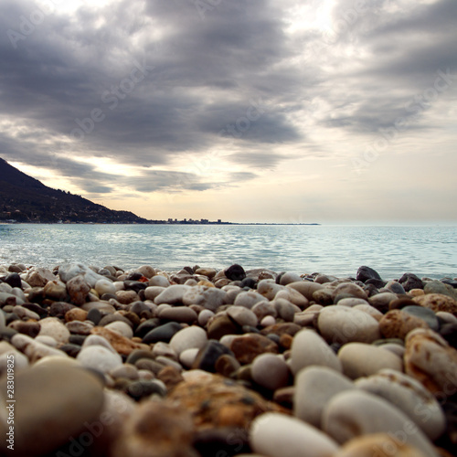 Calm water at coast. Ripple of water near shoreline. Silhouette of city on skyline. Stone seashore before storm. Rocky beach near the bay.