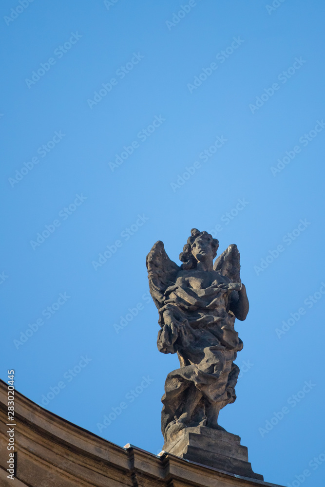 Statue on roof of St. Francis of Assisi church in Prague with blue sky in background