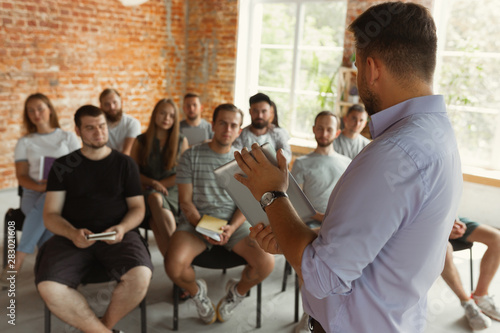 Male speaker giving presentation at university workshop. Audience or conference hall. Using tablet and flipchart for visualisation of information. Scientific conference event, training. Education.