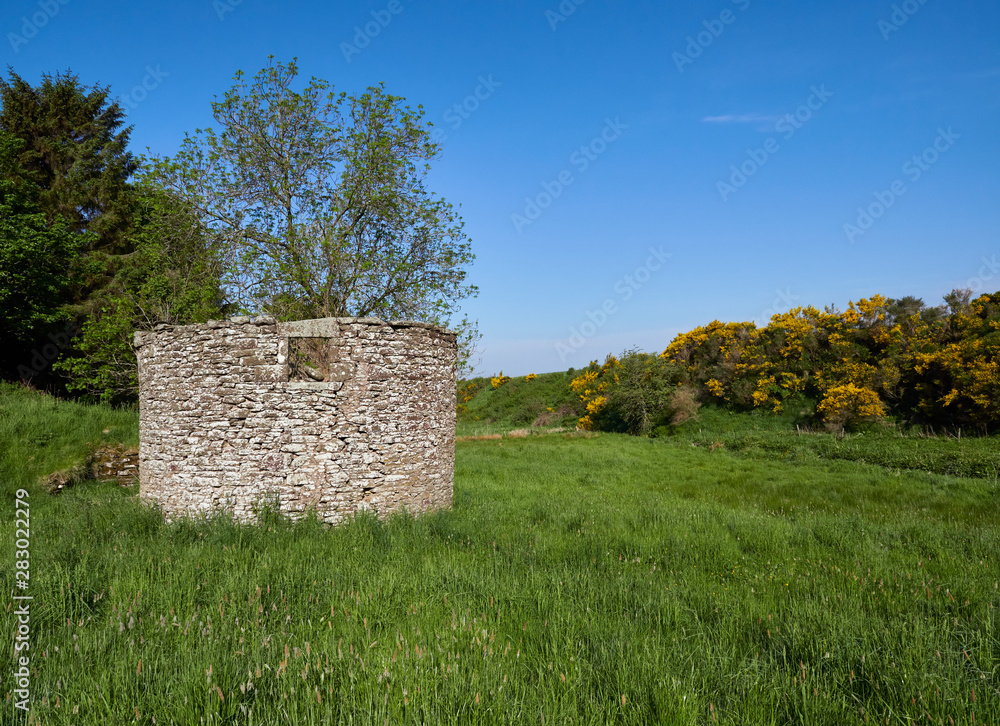 Looking end on at an old stone ruined building with a square window in a grass field in a small Valley near to Guthrie, Forfar, Angus in Scotland.