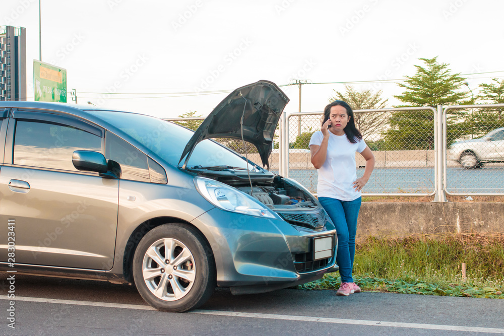 Asian teenage women holding a mobile phone Walking around the car, stressful mood during the evening hours. Along the highway Because her car broke down And she is waiting for help from someone.