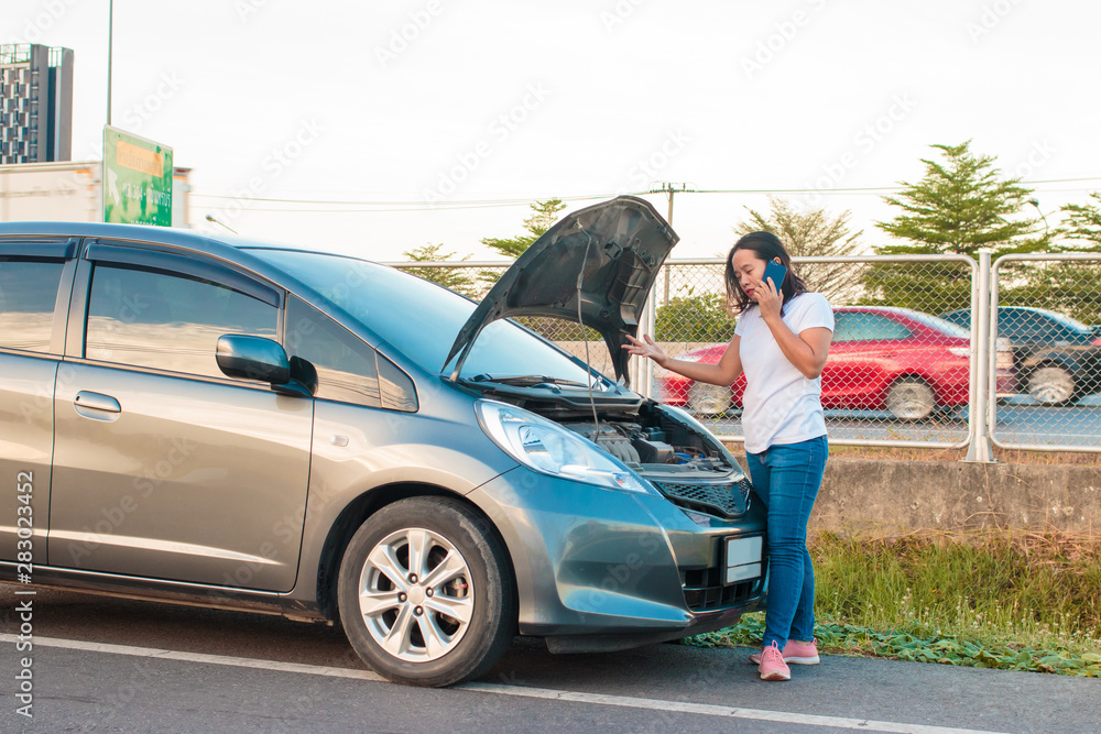 Asian teenage women holding a mobile phone Walking around the car, stressful mood during the evening hours. Along the highway Because her car broke down And she is waiting for help from someone. Asian teenage women holding a mobile phone Walking around the car, stressful mood during the evening hours. Along the highway Because her car broke down And she is waiting for help from someone.