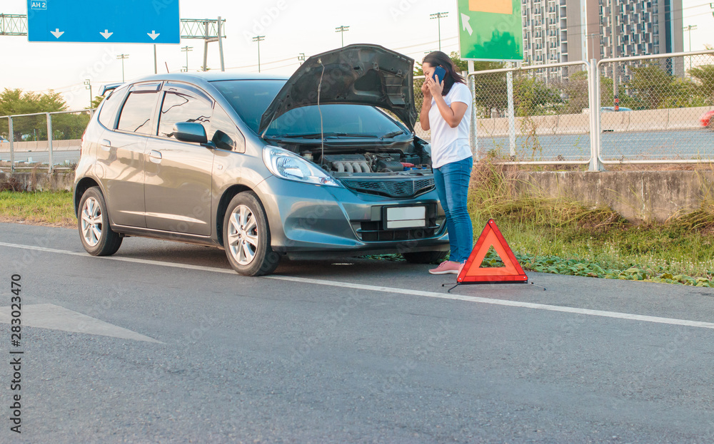 Asian teenage women holding a mobile phone Walking around the car, stressful mood during the evening hours. Along the highway Because her car broke down And she is waiting for help from someone. Asian teenage women holding a mobile phone Walking around the car, stressful mood during the evening hours. Along the highway Because her car broke down And she is waiting for help from someone.