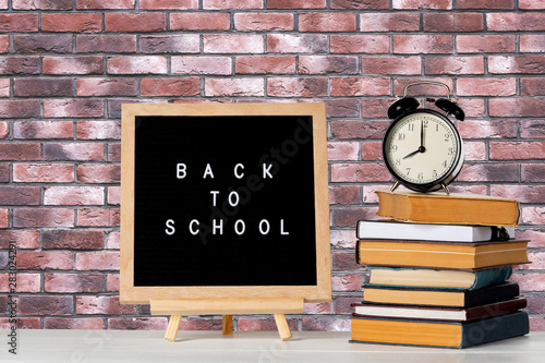 Back to school words on a letter board with books and vintage alarm clock against brick wall background.
