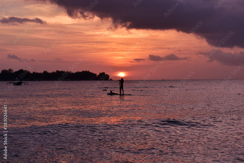 Indonesian man paddling on the strait between Gili Meno and Gili Trawangan Islands in sunset, Lombok, Indonesia
