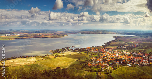 The Nové Mlýny Dam on the Dyje River.  Moravian village (Pavlov) with a dock at a large lake, around a vineyard, the sun illuminates the landscape in gold through white clouds in the blue sky photo