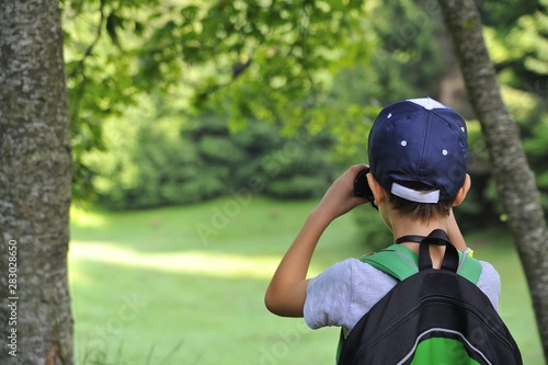 young child explores the nature of the woods and observes the animals of the forest with binoculars © kromatika