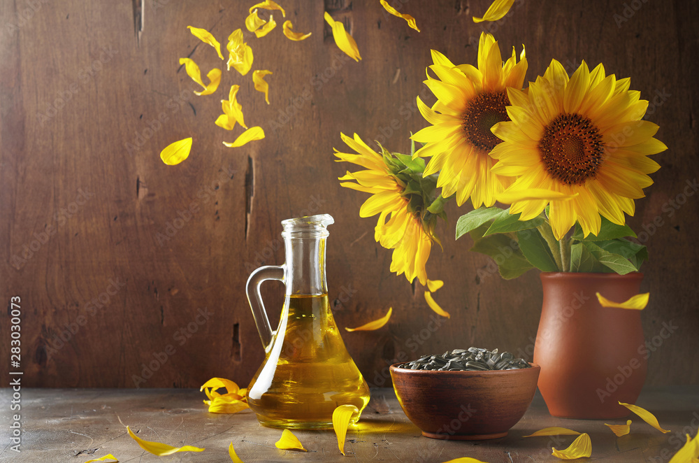 Still life of glass bottle with sunflower oil, seeds and flowers in ceramic vase