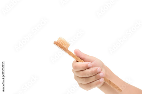 Children's hand holds a bamboo toothbrush on a white isolated background