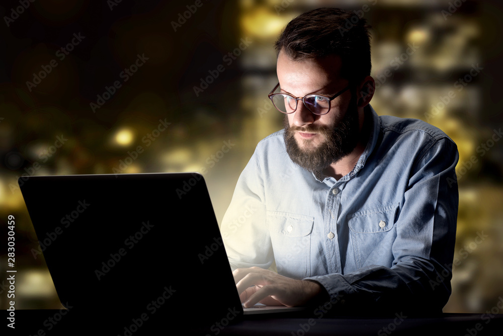 Young handsome businessman working late at night in the office with city lights in the background Young handsome businessman working late at night in the office with city lights in the background