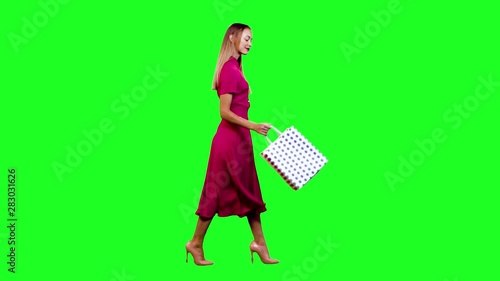 Cheerful shopper looking into her shopping bags and smiling happily while walking in full shot over green screen.