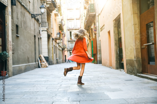 Beautiful girl spinning around in the old city. Hipster travelling. Happy tourist dancing. Woman in orange stylish dress. Hair in the wind.