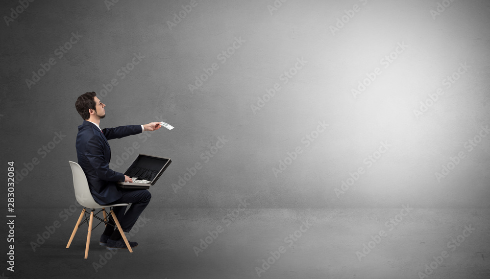 Businessman staying in an empty grey dark room with stuffs on his lap Businessman staying in an empty grey dark room with stuffs on his lap