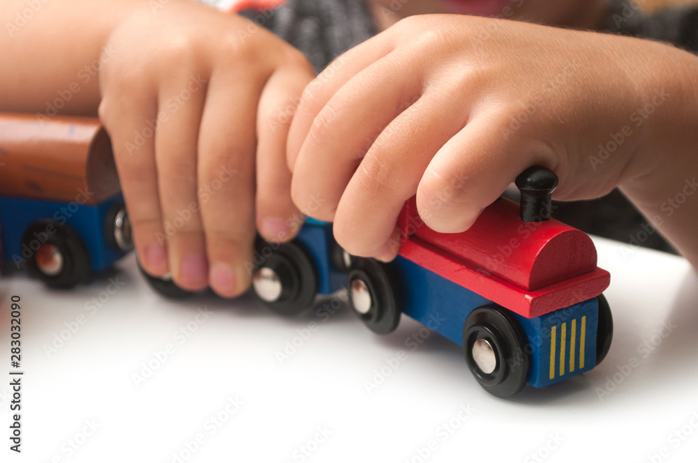 Closeup of hand of kid playing with wooden train on white background