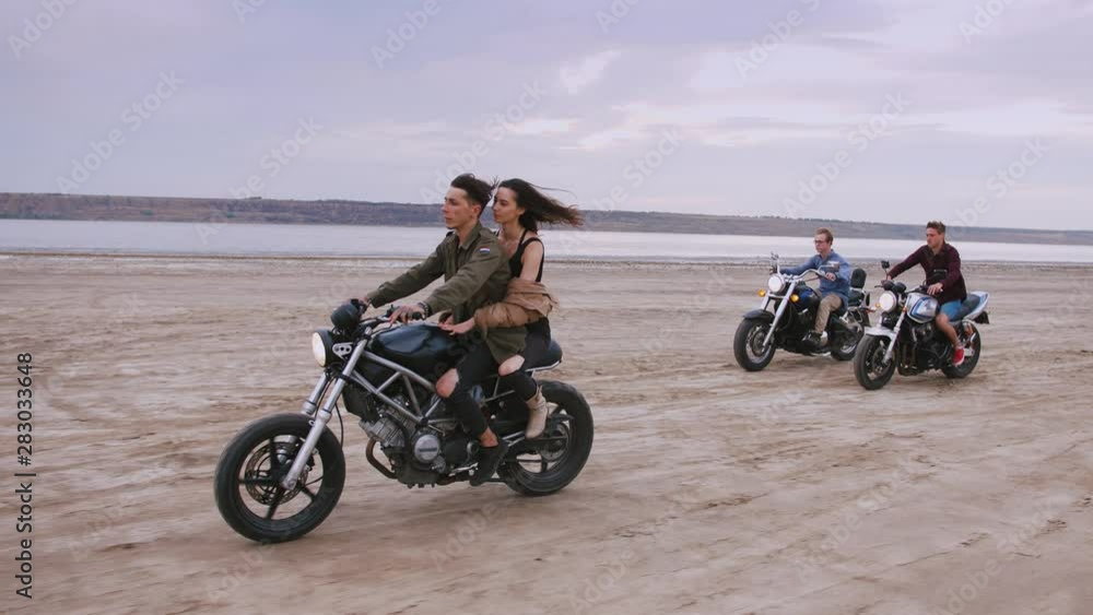 Group of young people riding motorbikes on the beach in evening. slow motion Group of young people riding motorbikes on the beach in evening. slow motion