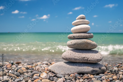 pyramid of sea pebbles on the beach against the backdrop of the sea wave in sunny day. concept of balance harmony and meditation. copy space