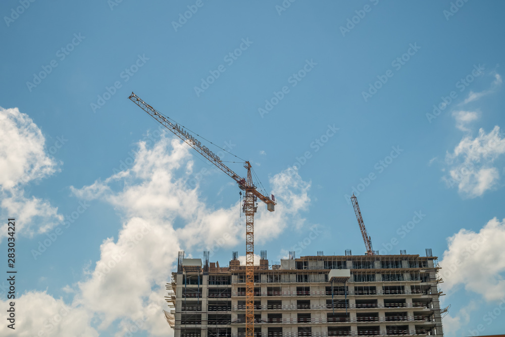 The construction of a multistory building against the blue sky, stands next to a yellow tower crane. Photo bottom up The construction of a multistory building against the blue sky, stands next to a yellow tower crane. Photo bottom up
