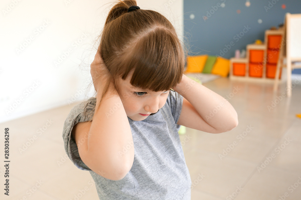 Sad little girl with autistic disorder covering ears with hands in playroom Stock Photo Adobe