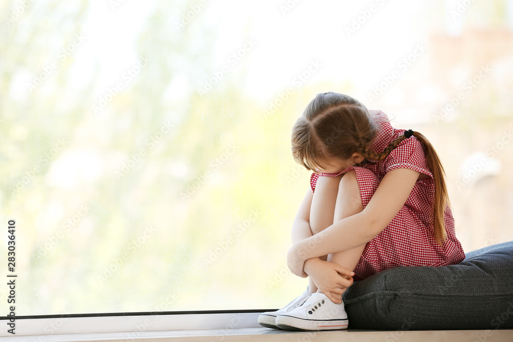 Sad little girl with autistic disorder sitting on window sill at home ...