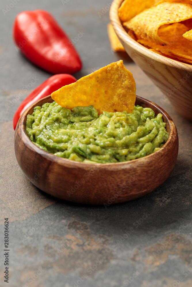 close up view of Mexican nachos with guacamole and chili peppers on stone table close up view of Mexican nachos with guacamole and chili peppers on stone table