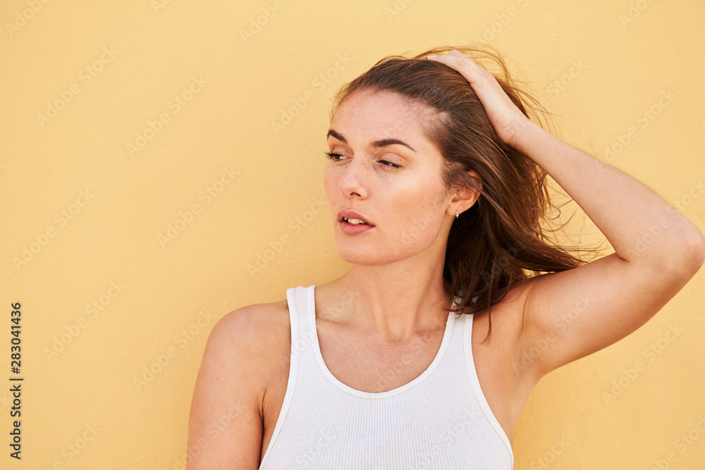 Stunning young brunette in white against yellow wall, looking away Stunning young brunette in white against yellow wall, looking away