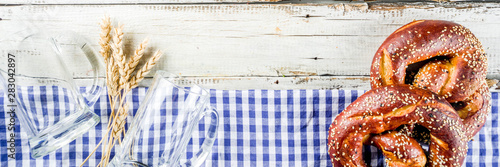 Oktoberfest festive background with traditional Bavarian checkered tablecloth, pretzels and beer mugs.