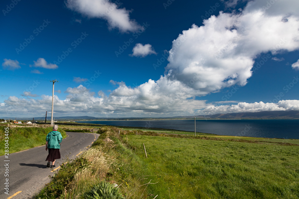 senior woman walking on rural road on the west coast of County Kerry, Ireland, scenic landscape senior woman walking on rural road on the west coast of County Kerry, Ireland, scenic landscape