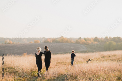 Samesex caucasian lesbian family with a child and a dog walking outdoors on the background of beautiful nature. Mothers having fun with their son. © anna_gorbenko