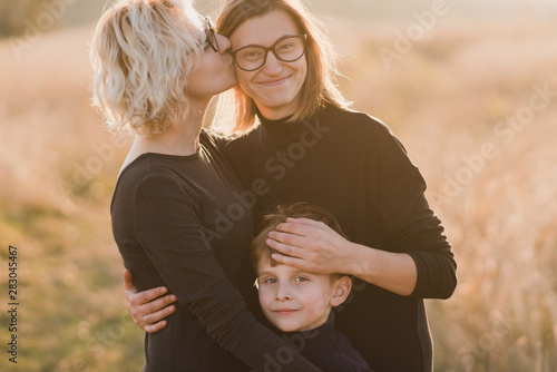 Samesex caucasian lesbian family with a child and a dog walking outdoors on the background of beautiful nature. Mothers having fun with their son. photo