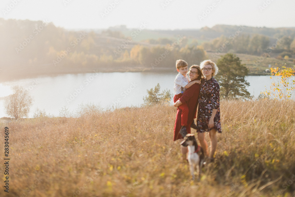 Samesex caucasian lesbian family with a child and a dog walking outdoors on the background of beautiful nature. Mothers having fun with their son. Samesex caucasian lesbian family with a child and a dog walking outdoors on the background of beautiful nature. Mothers having fun with their son.