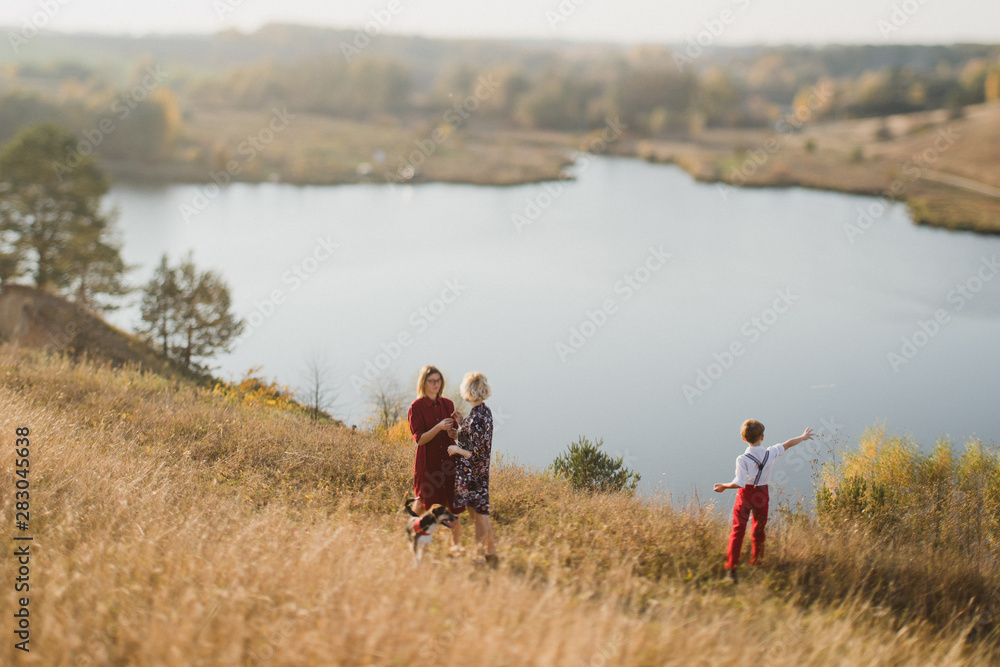 Samesex caucasian lesbian family with a child and a dog walking outdoors on the background of beautiful nature. Mothers having fun with their son.