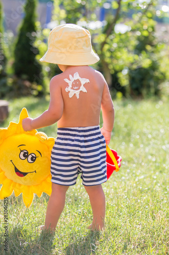 Toddler child with suntan lotion shaped as sun on his back, going at the beach with toys and flufy sun toy photo