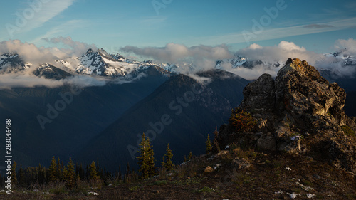 Olympic mountains in clouds in the background with a rocky peak in the foreground