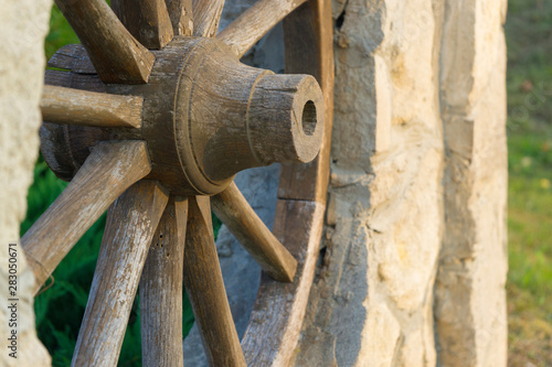 Fragment of an old wooden cartwheel against a wall of natural stone. Close-up. Selective focus. Copy space. photo