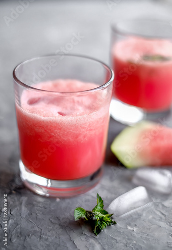 Glass of fresh watermelon lemonade with green leaf of mint at the gray cement background