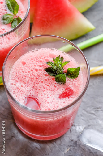 Glass of fresh watermelon lemonade with green leaf of mint at the gray cement background