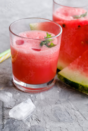 Glass of fresh watermelon lemonade with green leaf of mint at the gray cement background