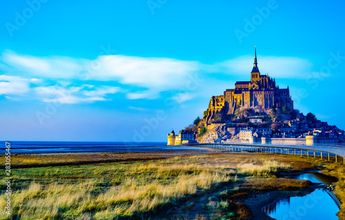 Beautiful medieval castle of Mont Saint Michel, France. The abbey, located on the island, is fenced with fortifications. The bridge goes to the island. Beautiful blue sky and fluffy white clouds. Dayt