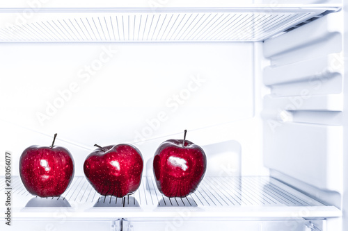 Three red apples is lying on the empty shelf of the fridge. Diet and weight loss concept.